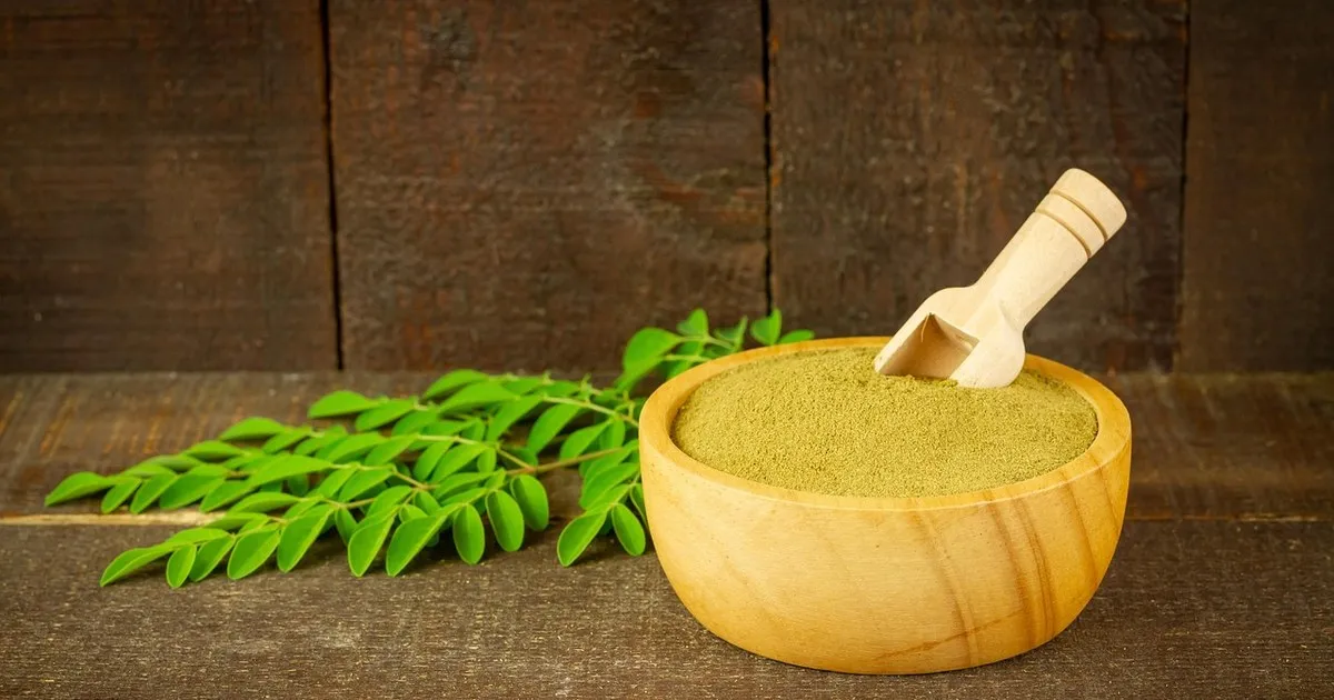 Moringa leaves and moringa leaf powder in a wooden bowl